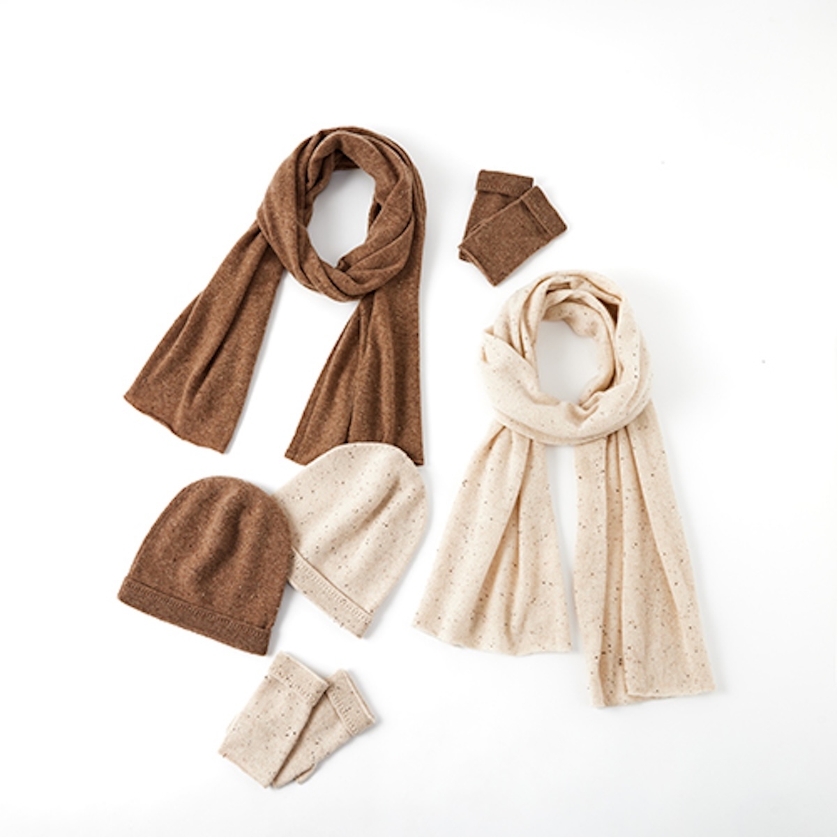 Flat lay of two cashmere scarves, two beanies and two pairs of wrist warmers on white