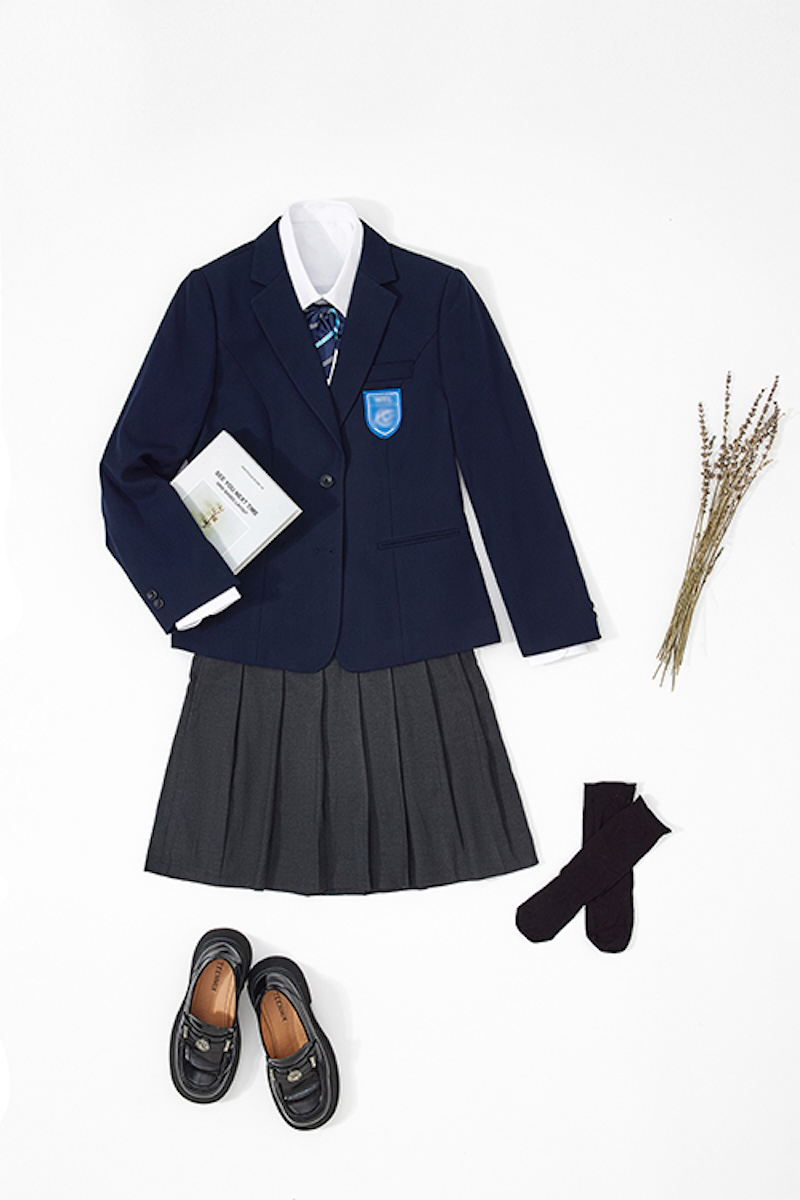 Flat lay of a school uniform: navy blazer, shirt, striped tie, pleated skirt and loafers