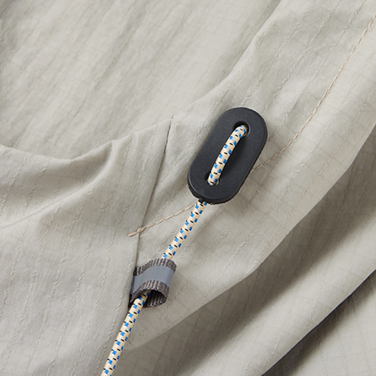 Close-up of a matte black cord lock and blue-flecked bungee cord on stone ripstop