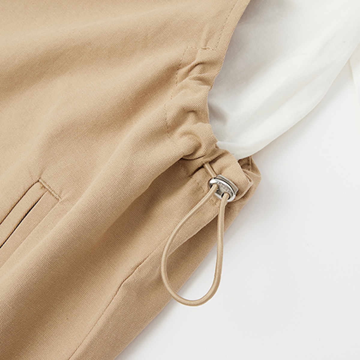 Side waist drawcord and metal toggle on a khaki pinafore dress, white background