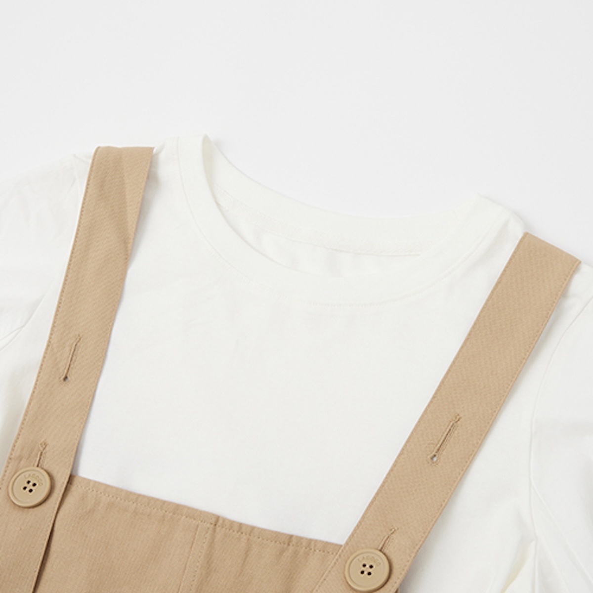 Detail of the white tee neckline and the wooden buttons on khaki pinafore straps