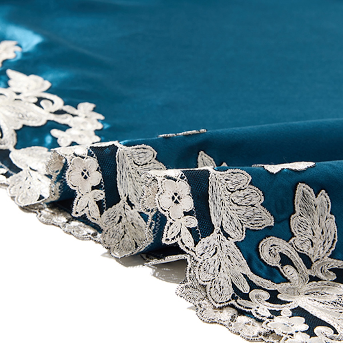 Close-up of ivory corded lace appliqué on the hem of a teal silk slip dress