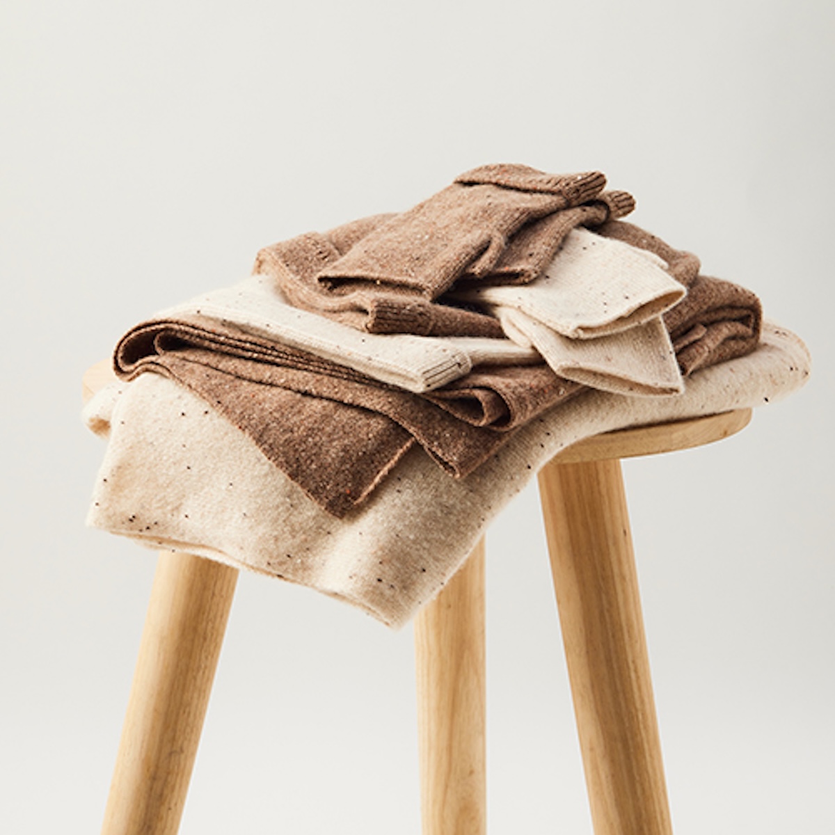 Cashmere knitwear folded on a wooden stool against a soft grey backdrop